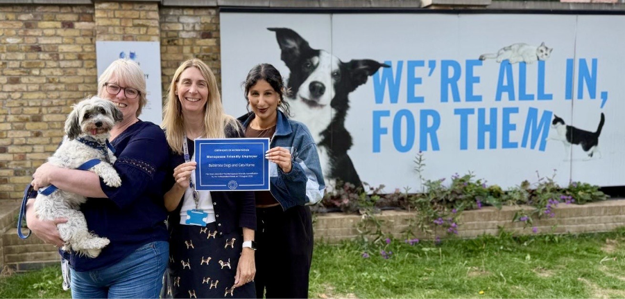 3 women standing in front of Battersea sign holding a dog. 