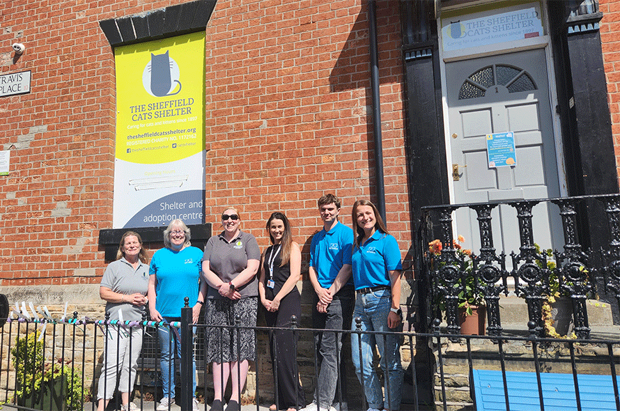 A group of people, including men and women, stands in front of a historic building, appearing friendly and welcoming.