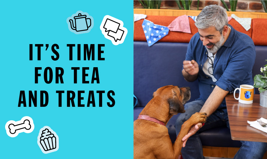 A man and his dog sit at a table with a sign that reads, It's time for tea and treats