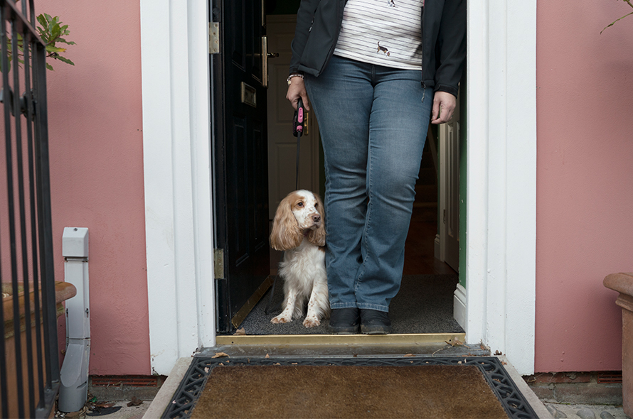 A person waits with their dog on a lead in a doorway