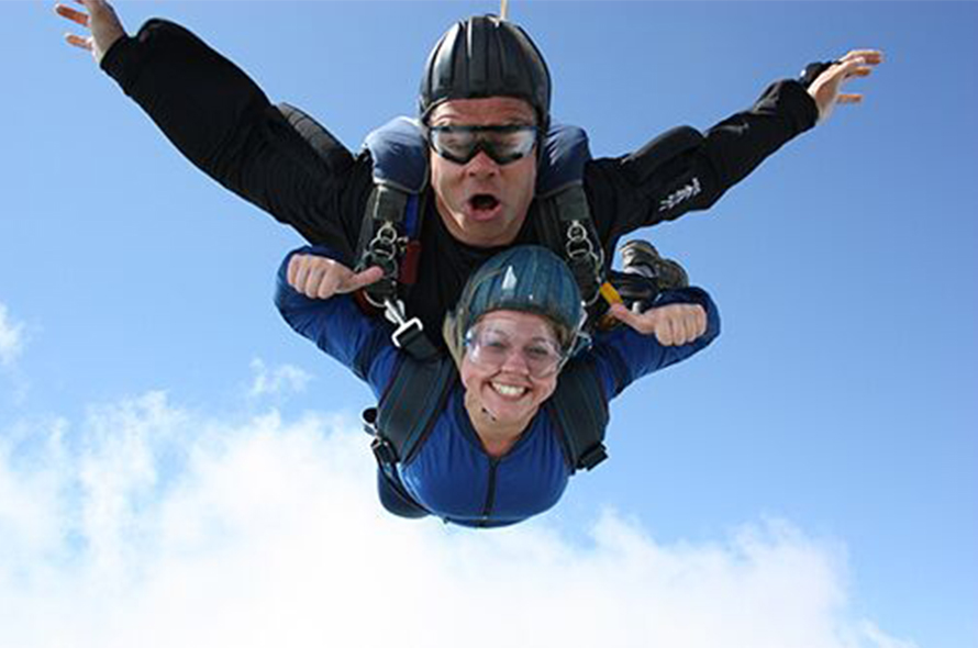 A skydiver and an instructor hold thumbs up while skydiving