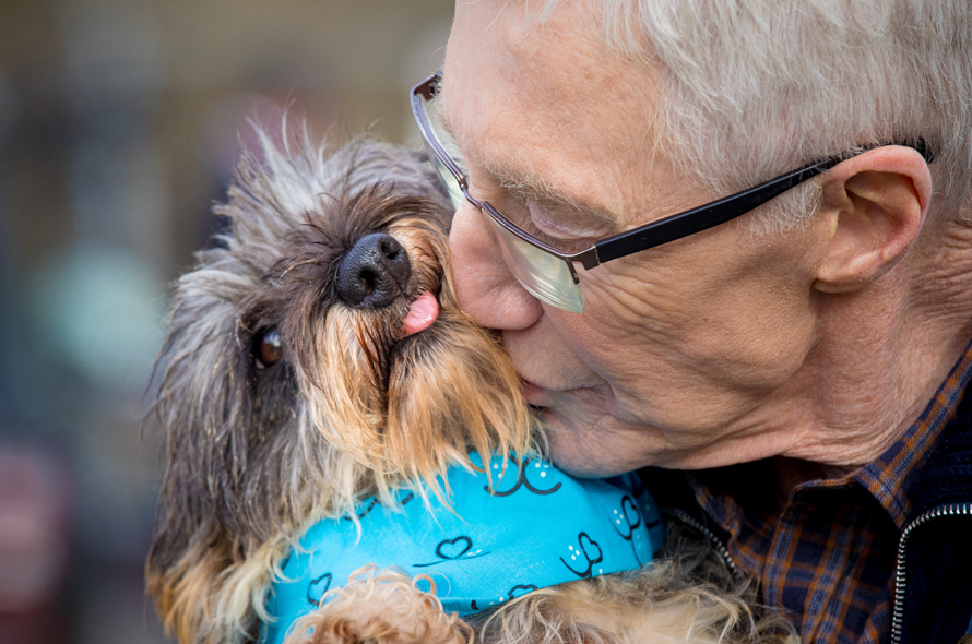Paul O'Grady nuzzles and a small brown dog who has it's tongue out and is wearing a blue bandana