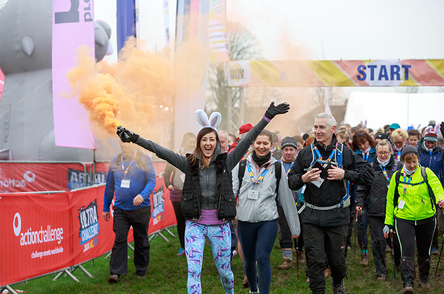 People walk together in a field, with bright orange smoke billowing around them, creating a striking visual scene.