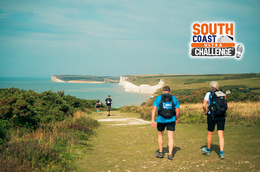  Two people trekking along a path, next to a sign that reads South Coast Challenge.