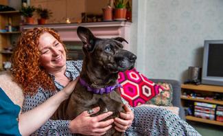 Woman sitting on couch with her arms around a brown dog