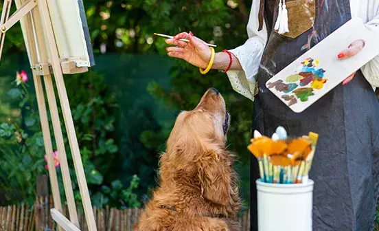 a person painting and a dog looking up at them