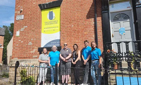 A group of people, including men and women, stands in front of a historic building, appearing friendly and welcoming.