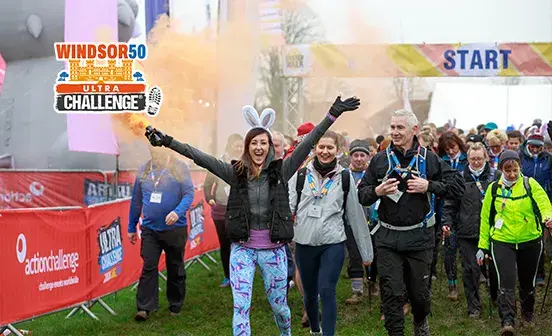 People walk together in a field, with bright orange smoke billowing around them, creating a striking visual scene.