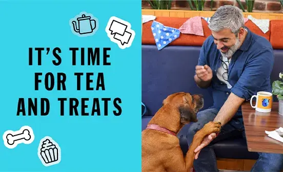 A man and his dog sit at a table with a sign that reads, It's time for tea and treats