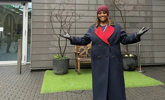 Alison Hammon standing with her arms open and smiling under the Battersea dogs and cats home sign
