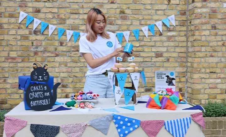 A person standing behind a cake and crafts sale