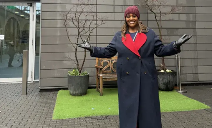 Alison Hammon standing with her arms open and smiling under the Battersea dogs and cats home sign